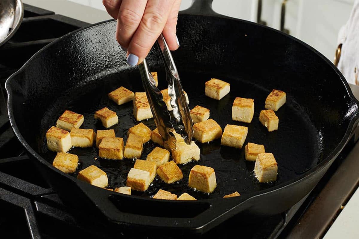 Frying tofu cubes in skillet on stove.