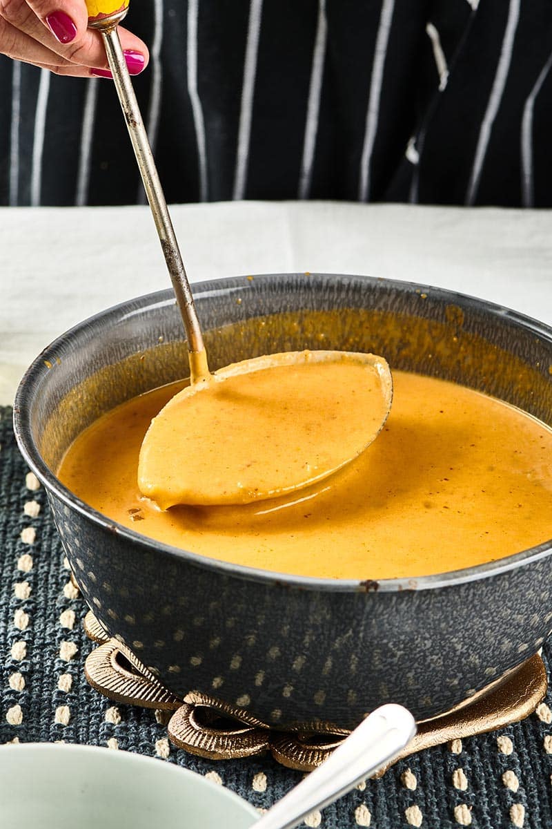 Ladle scooping Pumpkin Curry Soup from a pot.