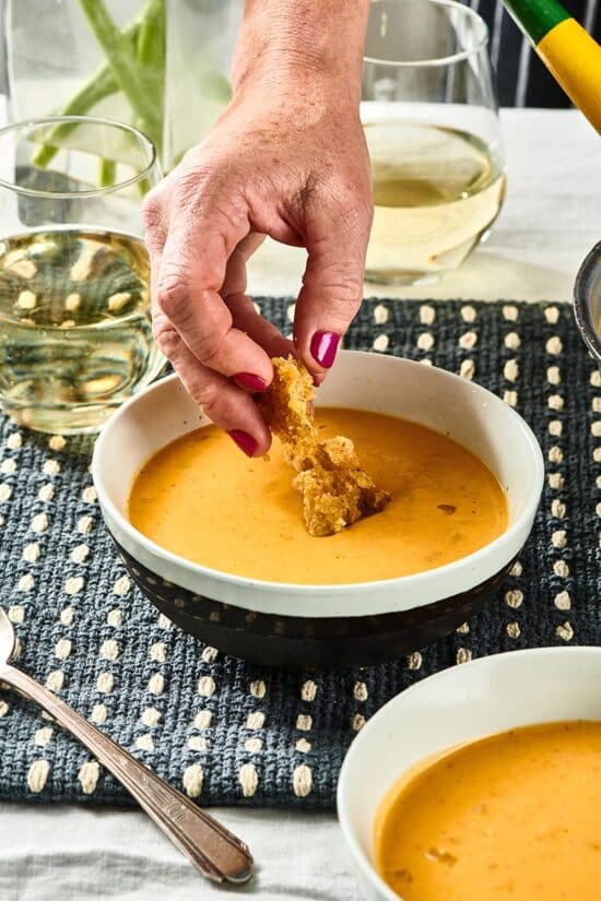 Woman placing croutons in a bowl of Pumpkin Curry Soup.