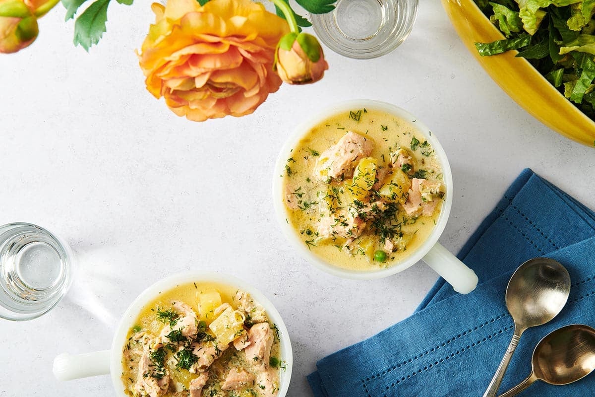 Two bowls of Salmon Chowder on a table with flowers, spoons, and blue cloth napkins.