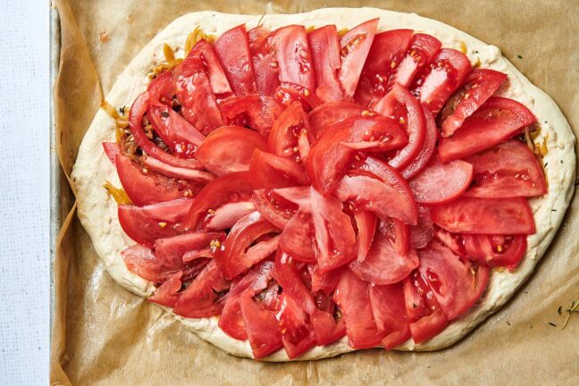 Raw pizza dough topped with tomato slices.