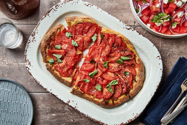 Partially-sliced Tomato Pie Pizza on a serving platter.
