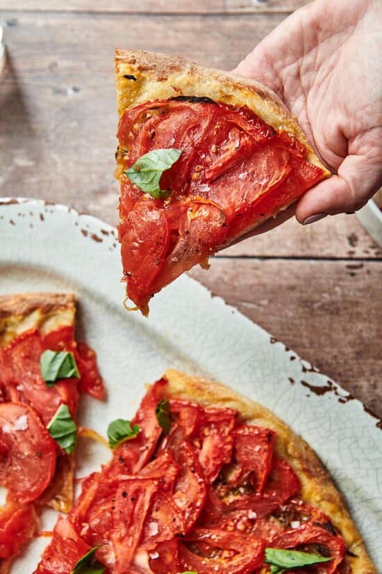 Hand holding a slice of Tomato Pie Pizza.
