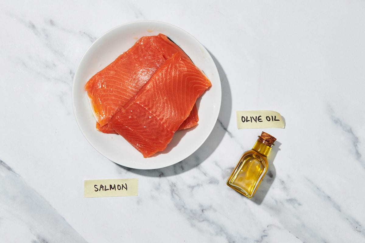 Fresh salmon filets and jar of olive oil on white marble.