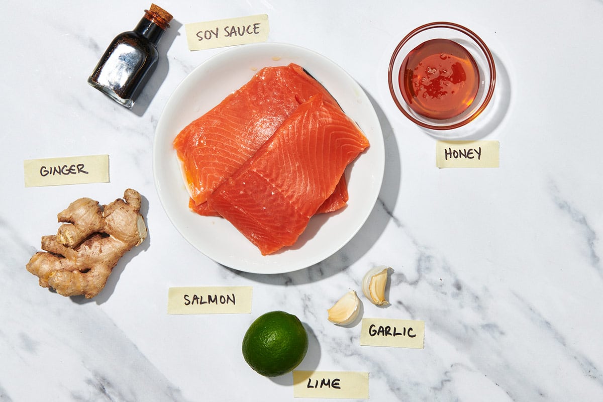 Fresh salmon filets, ginger, honey, and other ingredients on marble counter.