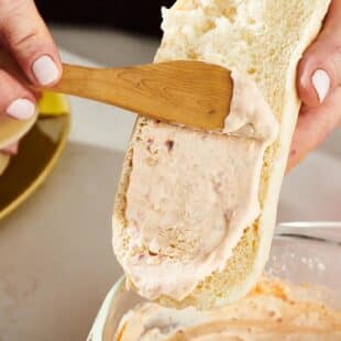 Wooden knife spreading Chipotle Mayo onto bread.