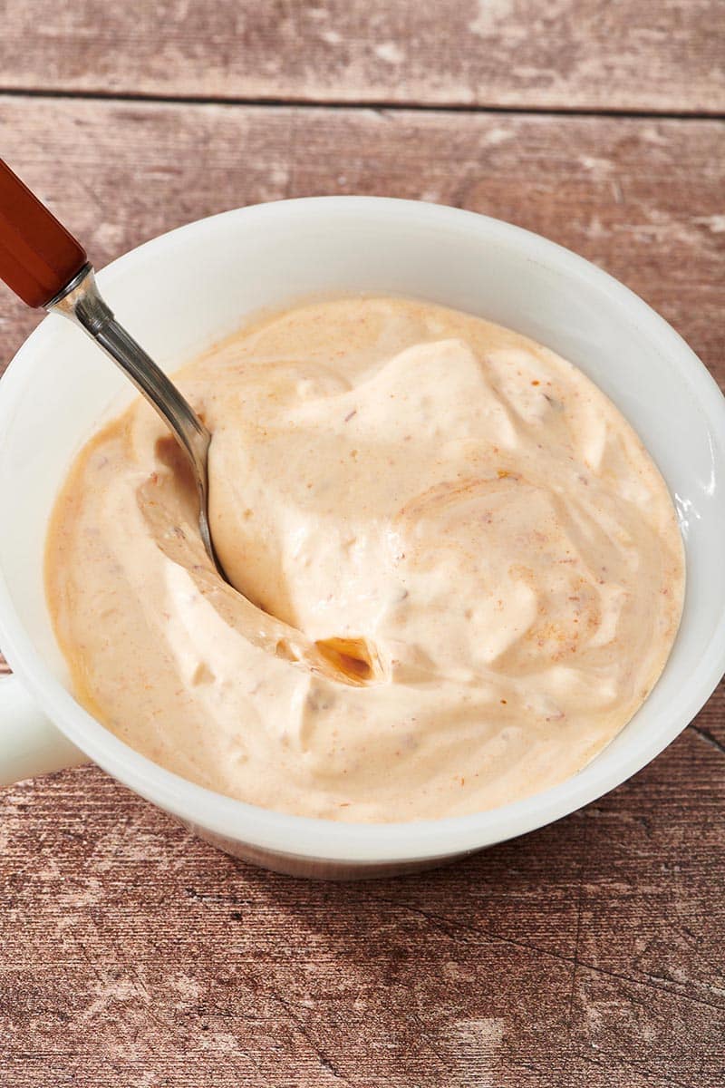 Spoon scooping Chipotle Mayo from a white bowl.