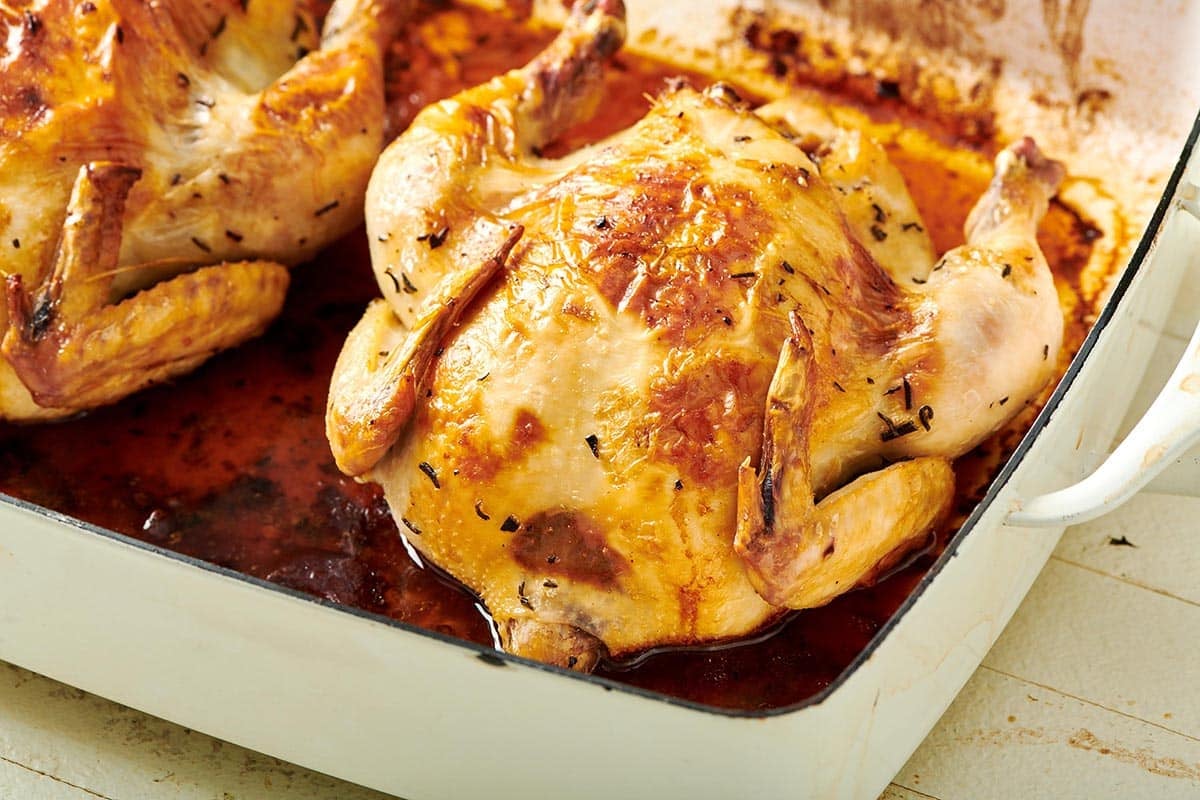 Roasted Cornish game hens in white baking pan on table.