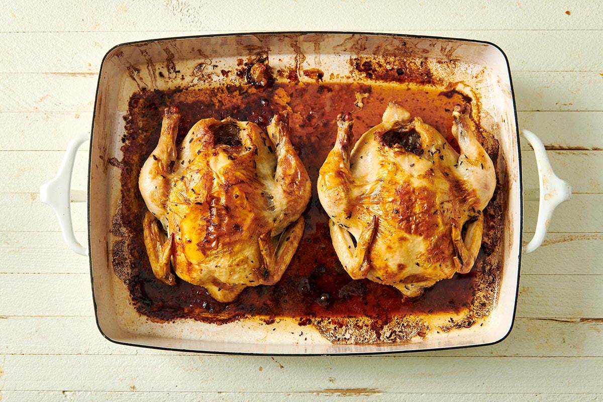 Two roasted Cornish game hens in baking dish on white table.