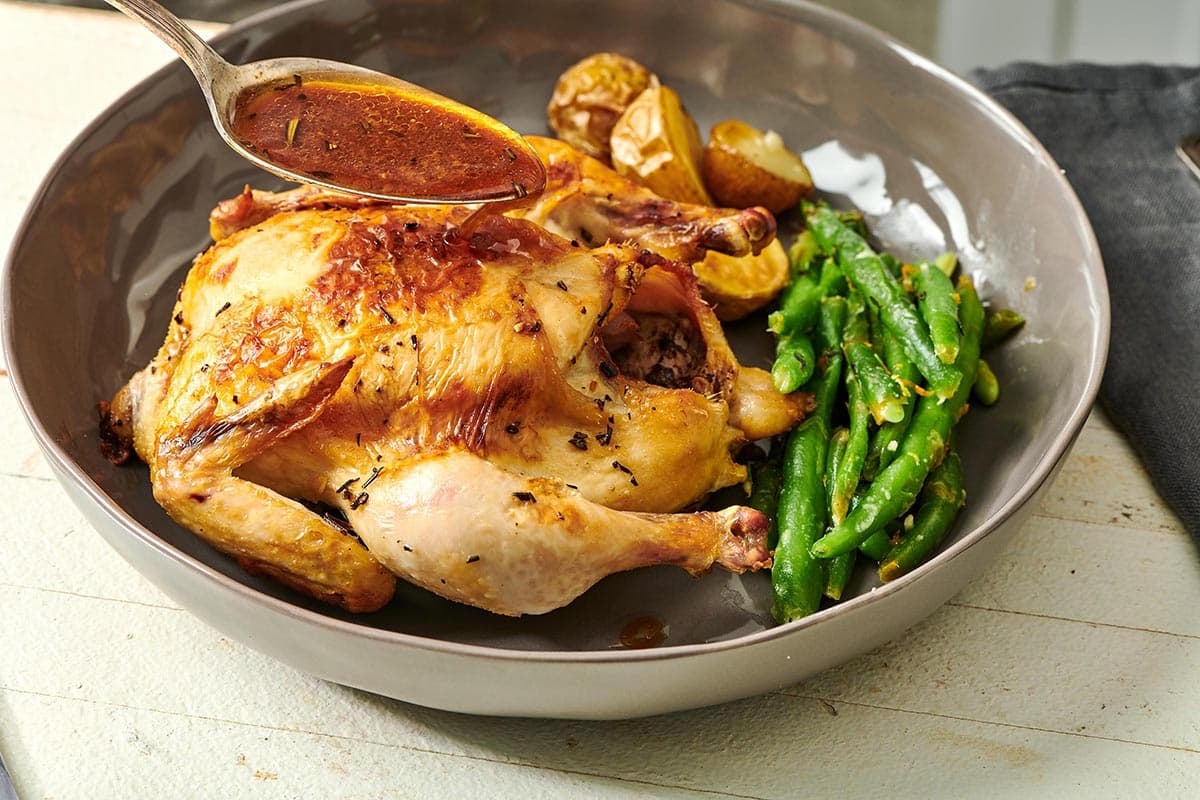 Adding sauce to roasted Cornish hen in bowl using spoon.