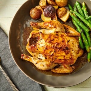 Cornish Hen on grey plate with green beans and roasted potatoes.