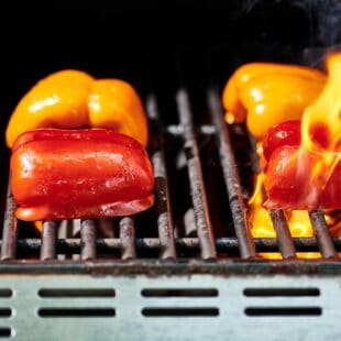Halved red and yellow peppers on a grill.