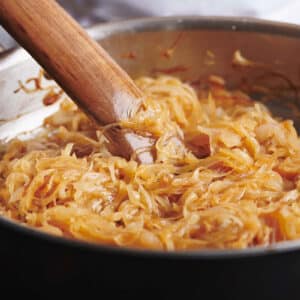 Pan of medium-brown onions being stirred by a wooden spatula.