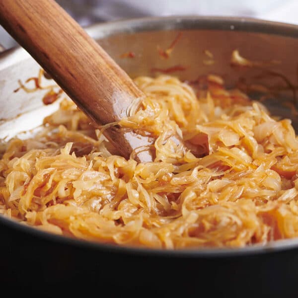 Pan of medium-brown onions being stirred by a wooden spatula.