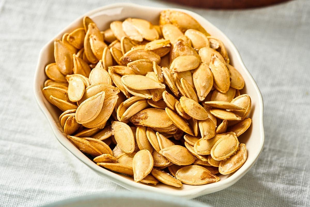 Small, white bowl filled with cooked pumpkin seeds.