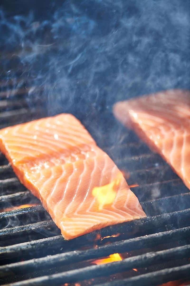 Salmon filets cooking on a smoky grill.