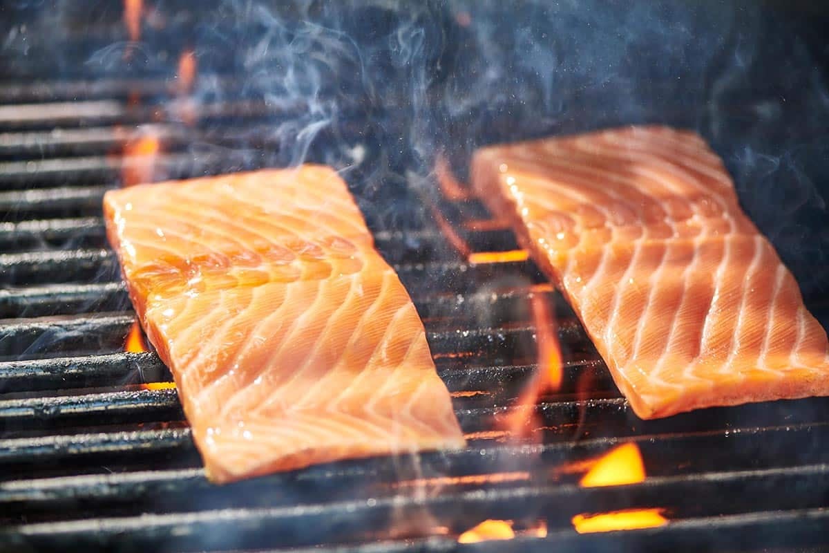 Two salmon filets cooking over flames on hot grill.