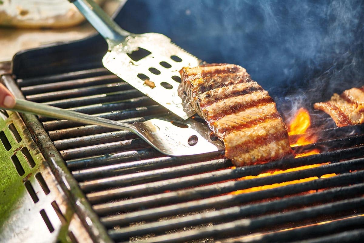 Flipping seared salmon filet with spatulas over fire on the grill.