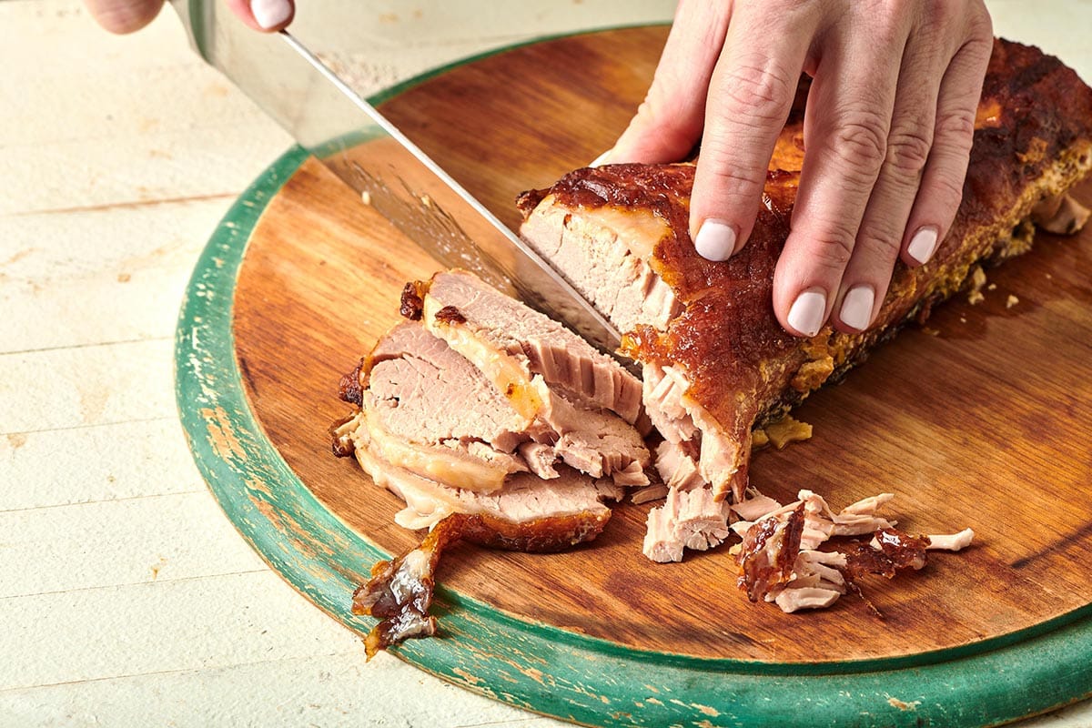 Woman slicing pork on a wooden cutting board.