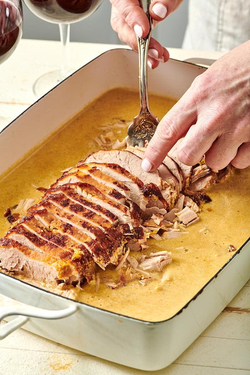 Woman using a fork to grab Milk Braised Pork from a baking dish.