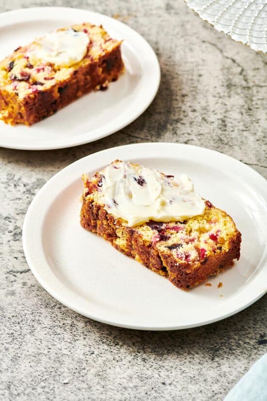 Slice of Orange Cranberry Bread with butter on a plate.