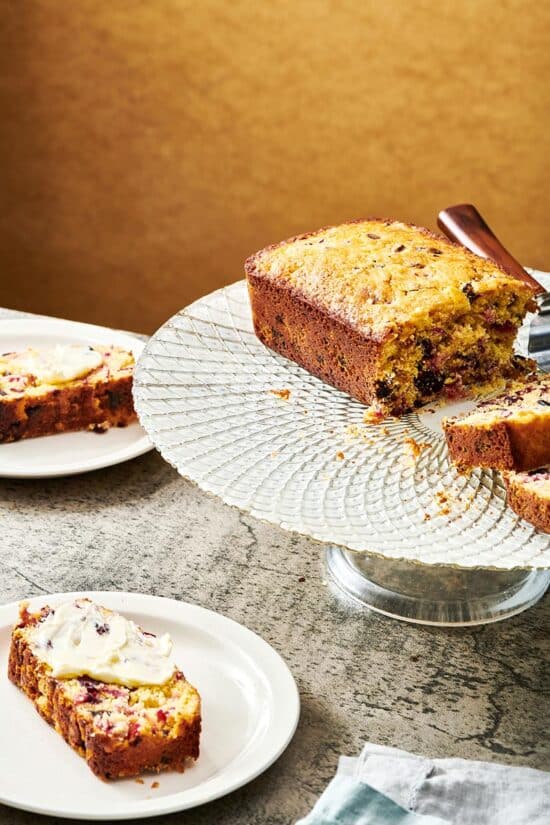 Partially-sliced loaf of Orange Cranberry Bread on an elevated serving platter.