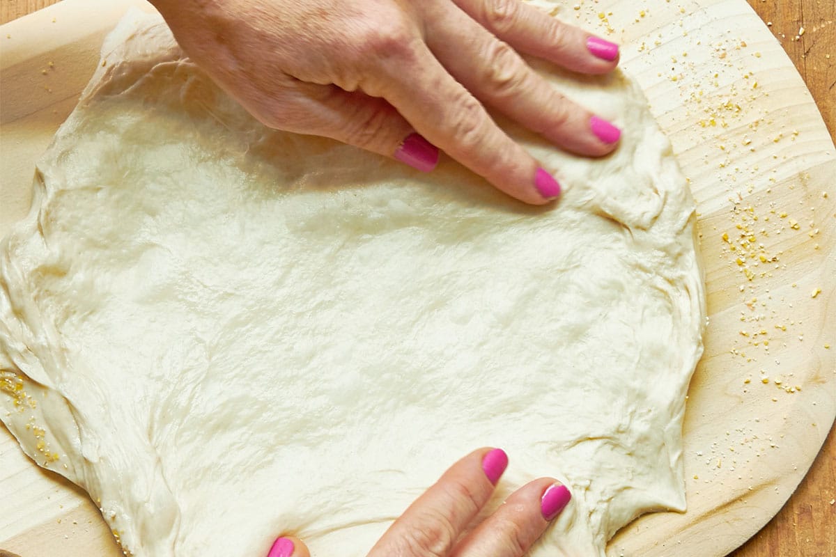 Woman forming pizza dough into a circle on wood board.