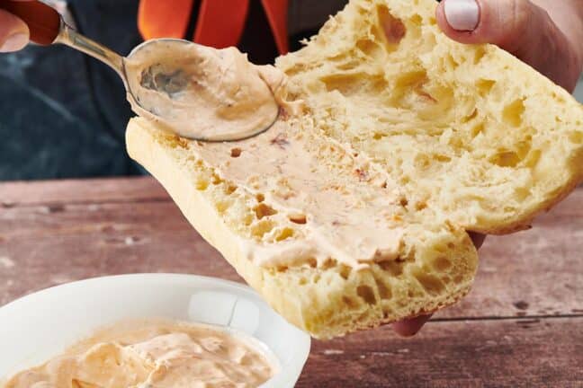Spoon spreading remoulade sauce onto bread.