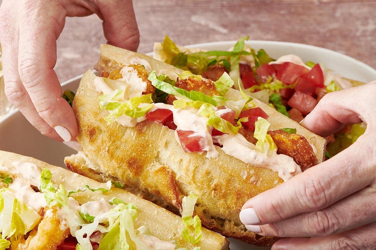Woman picking up shrimp po boy from serving dish.
