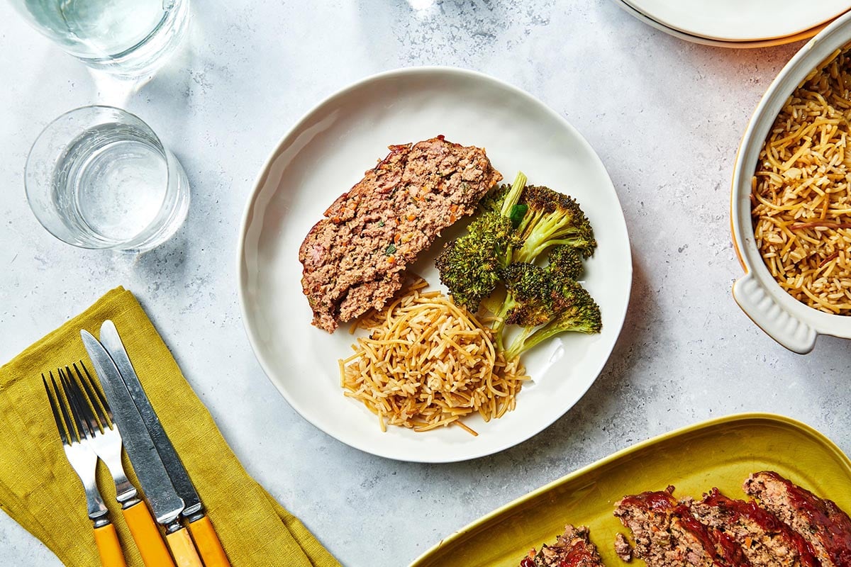 Plate of meatloaf, broccoli, and rice on a marbled table.