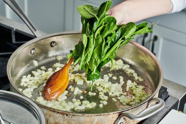 Handful of spinach being placed into a skillet of onions.