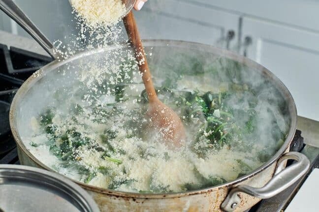 Parmesan cheese pouring into a steaming skillet of creamed spinach.