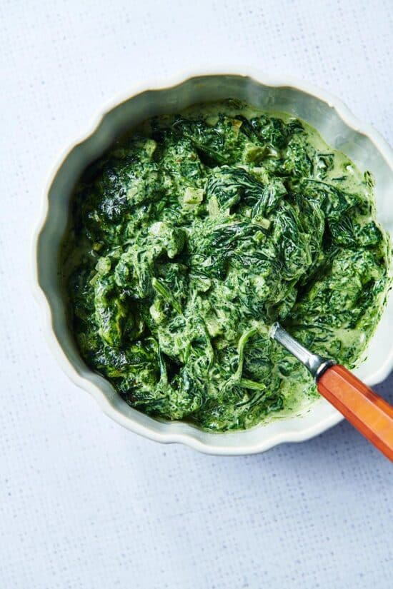 Spoon in a bowl of Creamed Spinach on a light table.
