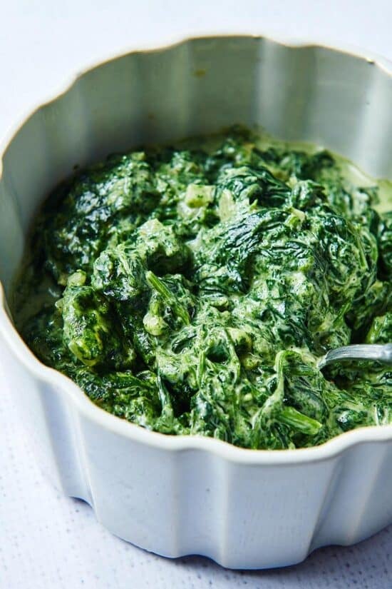 Spoon in a white serving dish of Creamed Spinach.