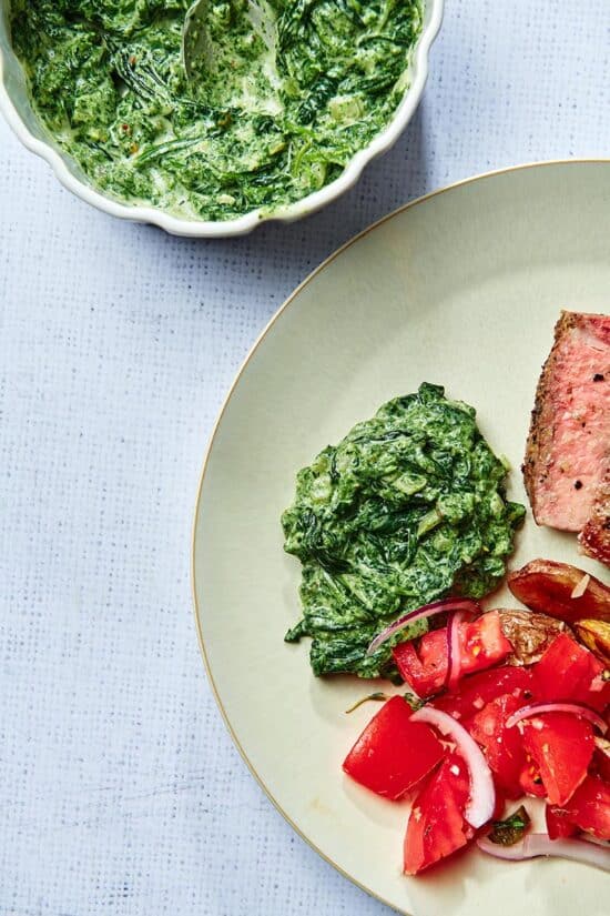 Creamed Spinach on a plate with meat and tomatoes.
