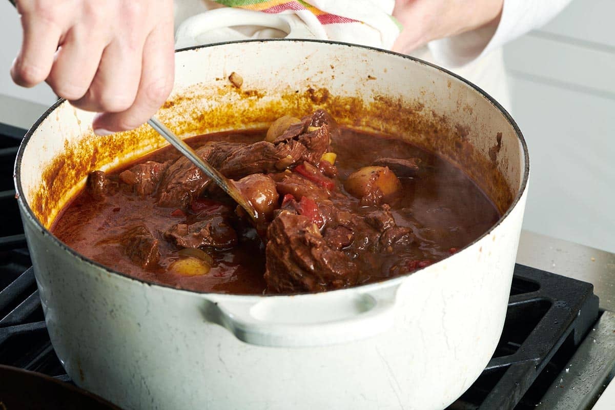 Stirring Hungarian goulash in large white pot on stove.