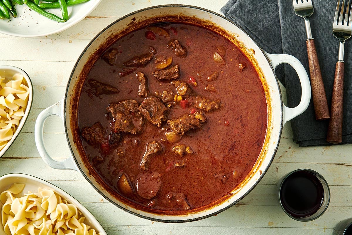Pot of Hungarian Goulash next to dishes of egg noodles.