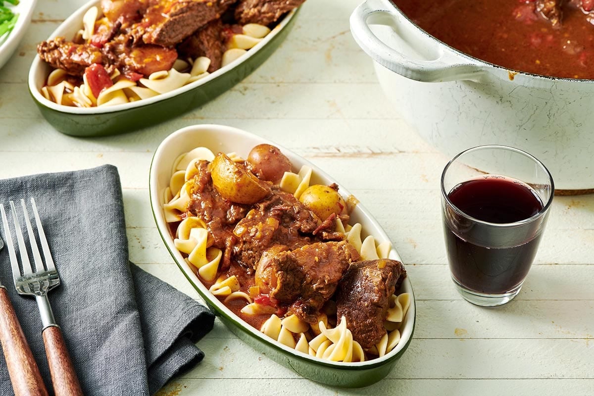 Oblong dish of Hungarian Goulash and egg noodles on a white table.