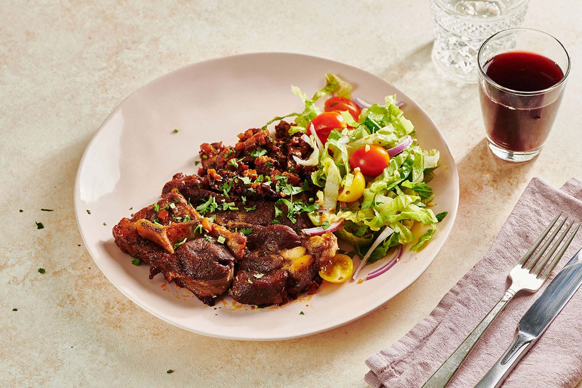Mediterranean Lamb Shoulder Chops on plain with wine glass and silverware.