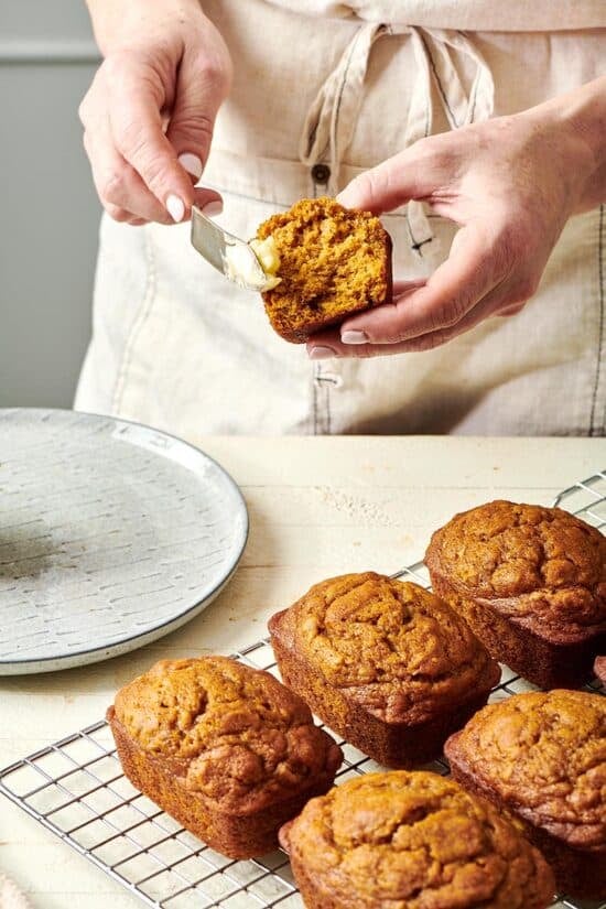 Woman putting butter on a Mini Pumpkin Bread Loaf.