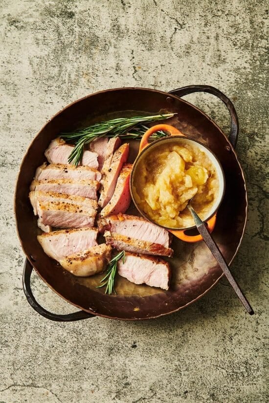 Bowl of apple sauce in a pan with slices of pork.