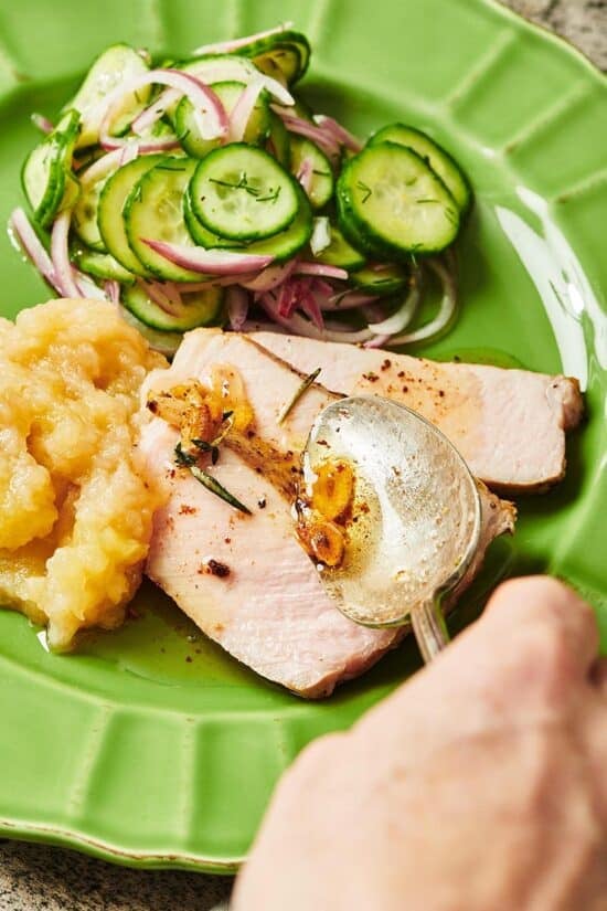 Spoon putting garlic butter on slices of cooked pork chops.