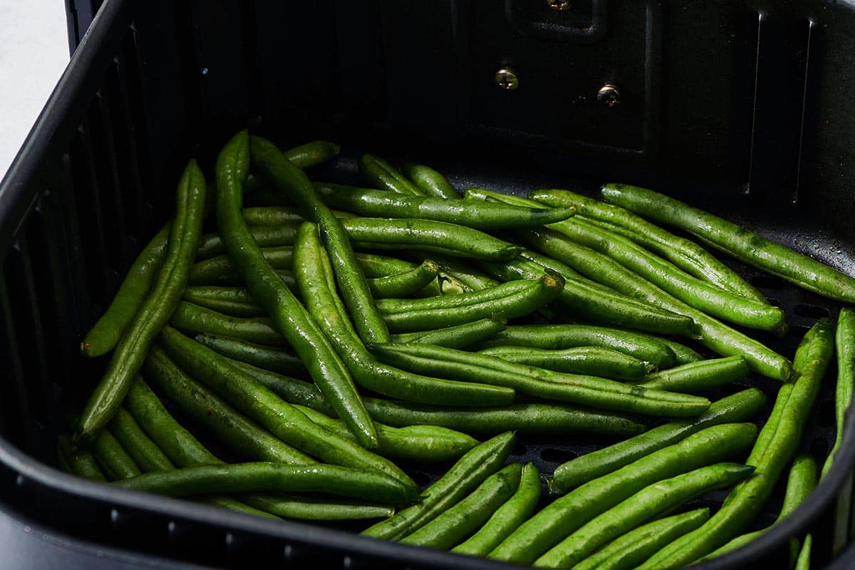 Uncooked Green Beans in a black air fryer basket.