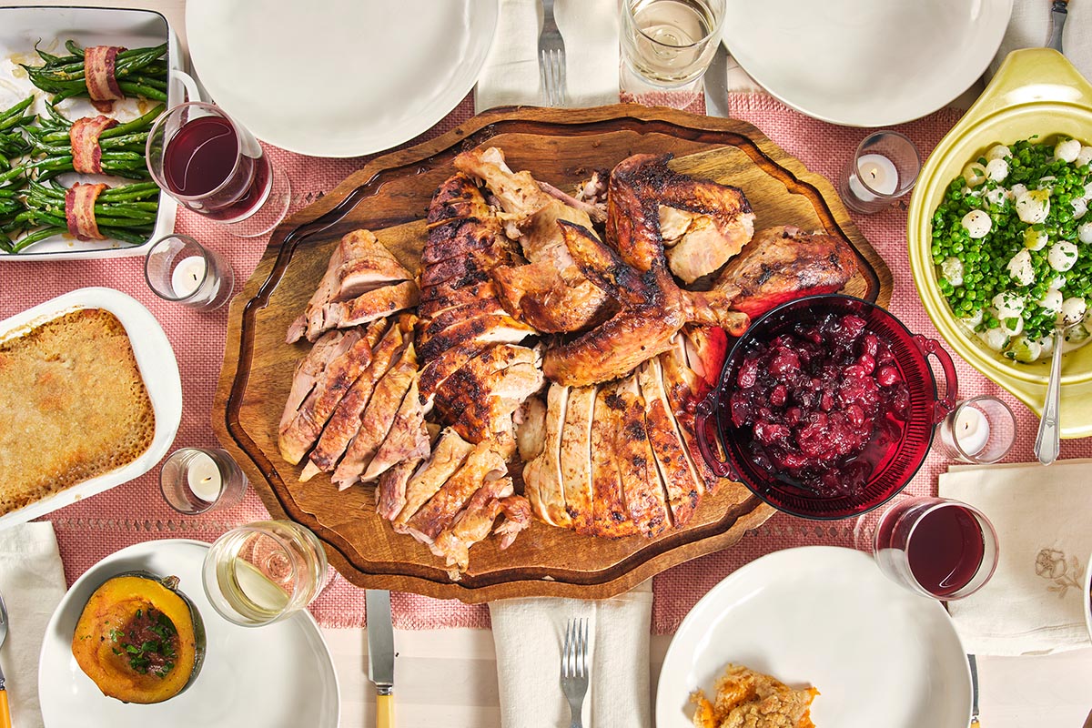 Wooden board of sliced Cajun Roasted Turkey on a table with plates, silverware, and glasses.