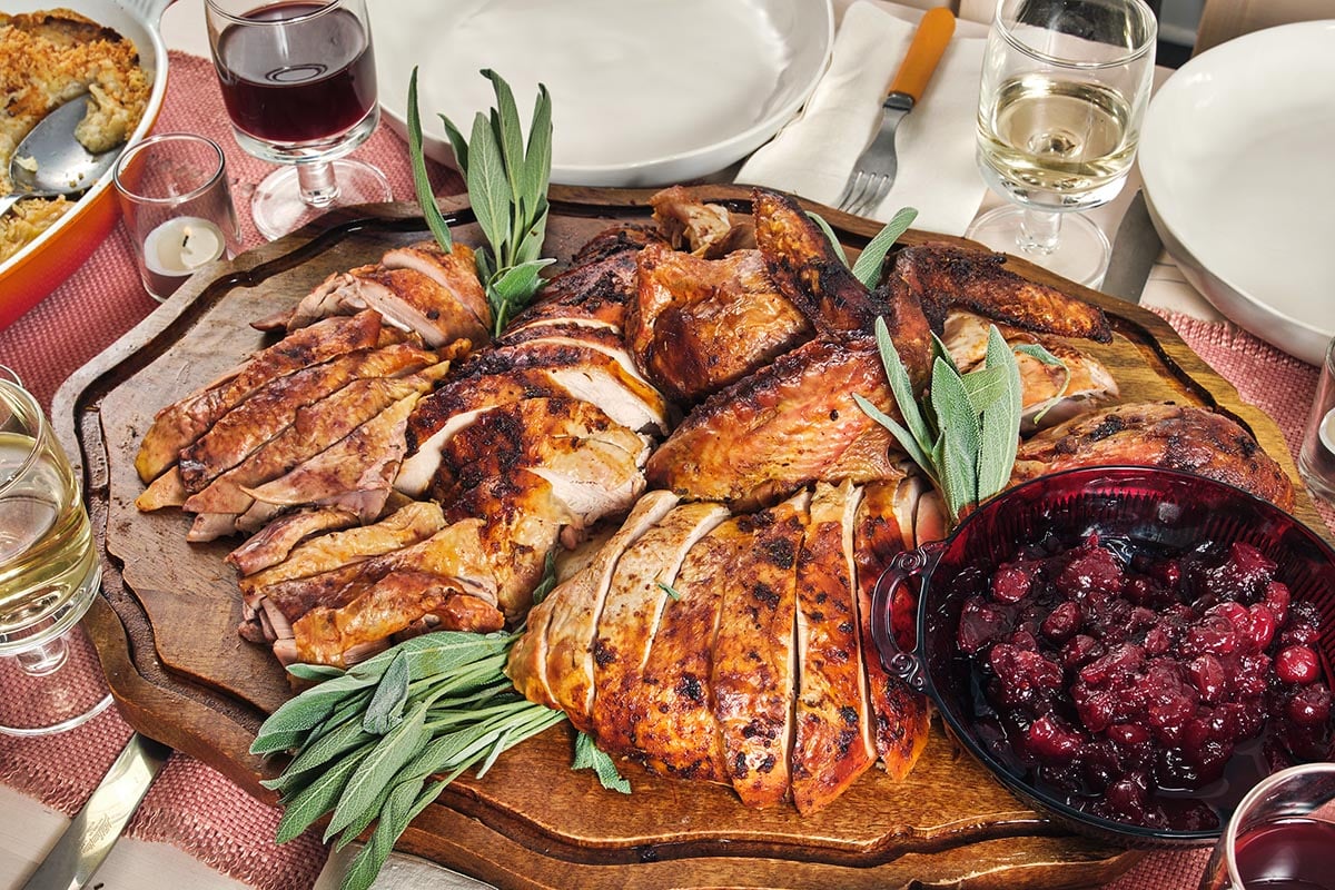 Sliced Cajun Roasted Turkey on a wooden board with a bowl of cranberry sauce.