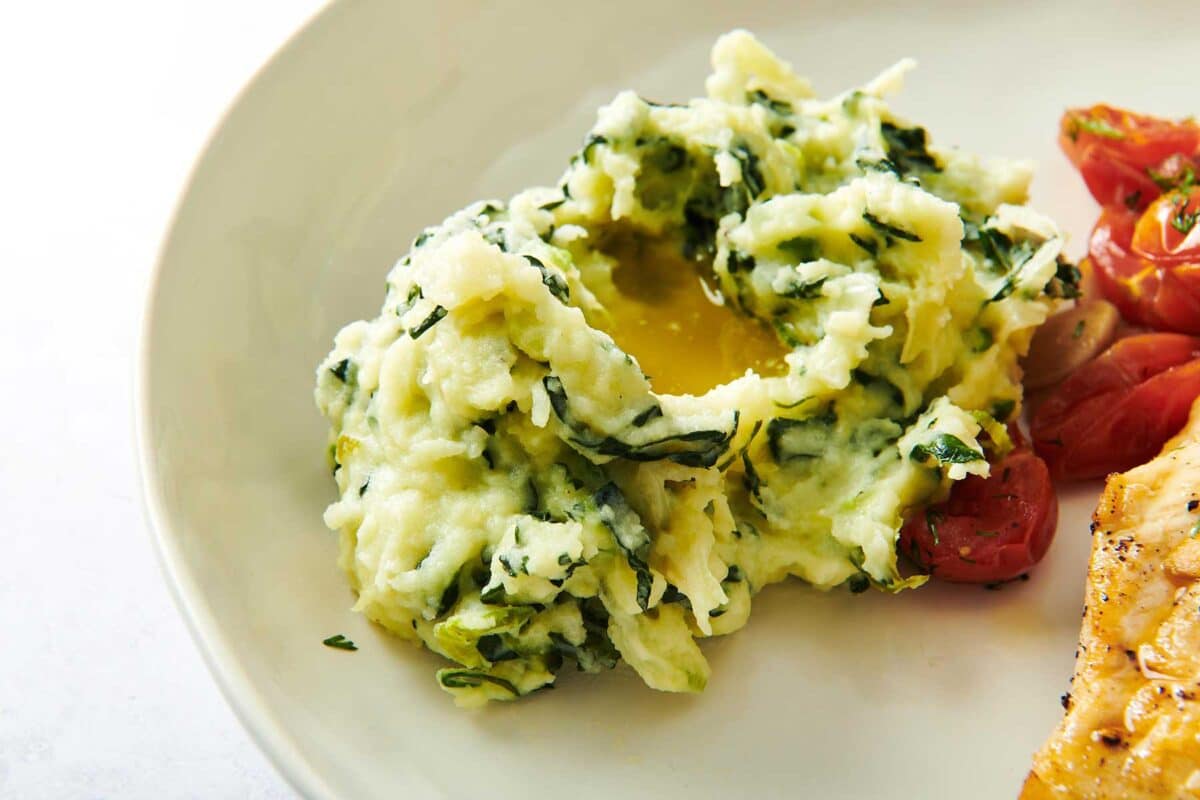 Mound of Colcannon topped with melted butter on a white plate.