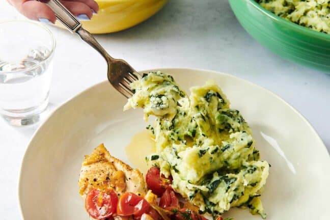 Fork scooping Colcannon from a plate set with tomatoes and chicken.