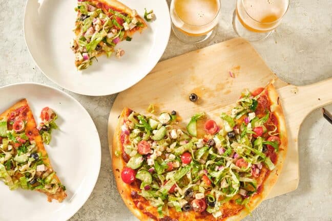 Greek Salad Pizza on two plates and a wooden board.