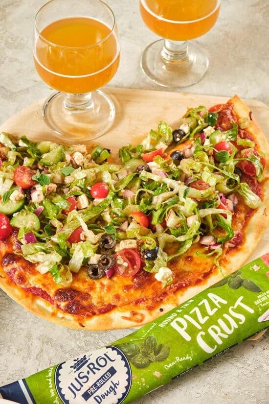 Partially-served Greek Salad Pizza on a wooden board.