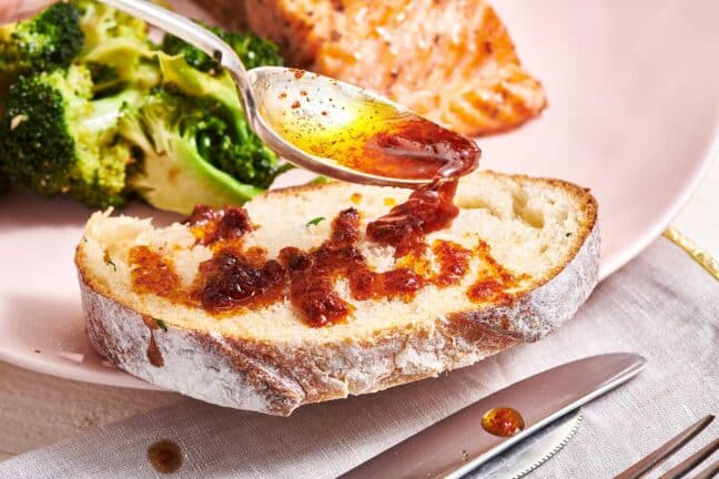 Spoon drizzling Harissa Sauce onto a slice of bread.